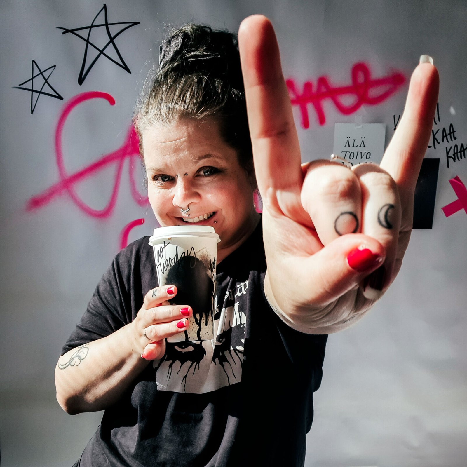 Aino Nieminen näyttää heavy metal -merkkiä graffitiseinän edessä